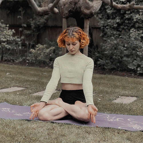 A woman sitting on her mat in a garden and meditating.